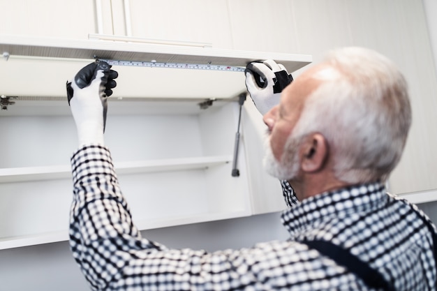 Senior klusjesman aan het werk in de keuken. Vernieuwing.