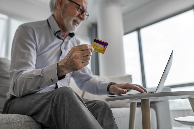 Senior knappe man zit thuis of op kantoor met behulp van laptopcomputer en creditcard voor online winkelen of betalen op het web