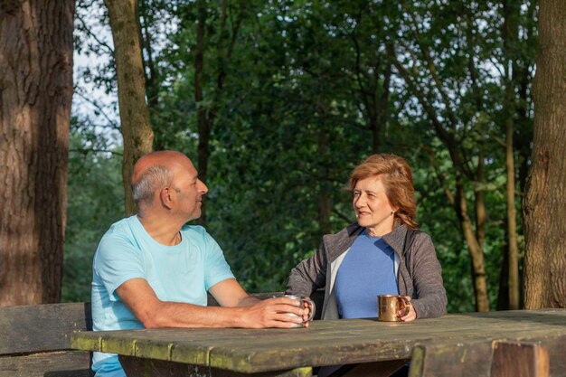 Senior koppel dat naar elkaar kijkt en glimlacht terwijl ze op een houten picknicktafel zitten te rusten