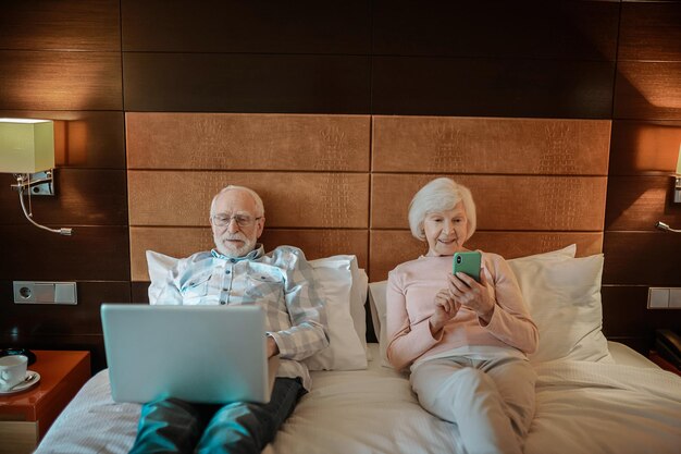 Senior koppel liggend in bed met hun gadgets in handen