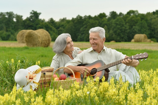 Senior koppel met gitaar op zomerveld met bloemen