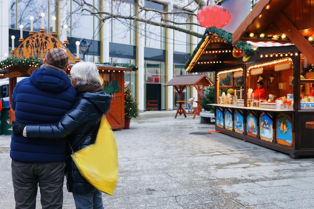 Foto senior koppel op de kerstmarkt in de kaiser-wilhelm-gedächtniskirche in winter berlijn, duitsland. advent fair decoratie en kraampjes met ambachtelijke artikelen op de bazaar.