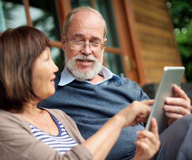 Senior koppel zit voor een houten hut en deelt een tablet