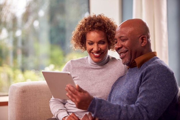 Senior koppel zittend op de bank thuis met behulp van digitale tablet kijken naar streaming film samen