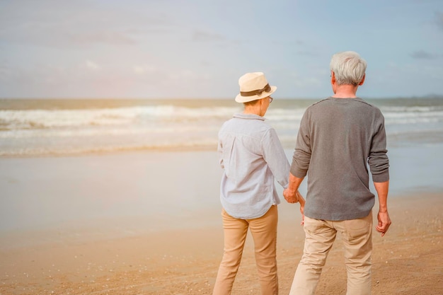 Senior koppels wandelen op het strand, hand in hand bij zonsondergang, plannen een levensverzekering bij pensioenconcept.