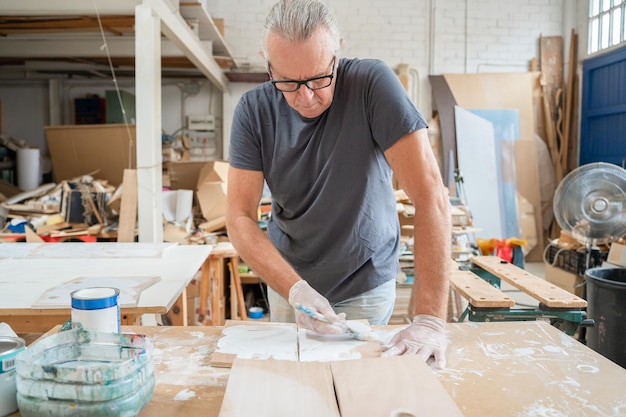 Foto senior kunstenaar werkt aan hout ambachten in een atelier schilderen houten meubels