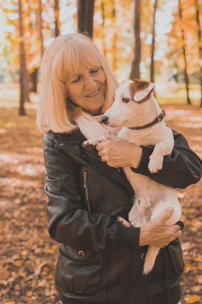 Senior lachende vrouw haar hond knuffelen in herfst park. actief ouder worden en huisdierconcept.