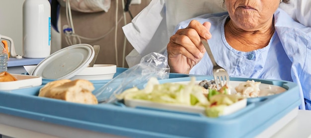 Senior lady in the hospital room sitting on the stretcher\
having lunch with the hospital food tray