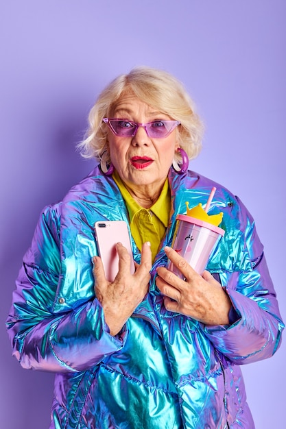 Photo senior lady is in shock by news message or like, stand using smartphone, isolated over purple space