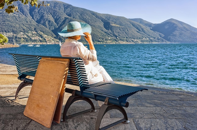 Senior lady sitting on the bench at the embankment of Ascona luxurious resort on Lake Maggiore, Ticino canton, in Switzerland.