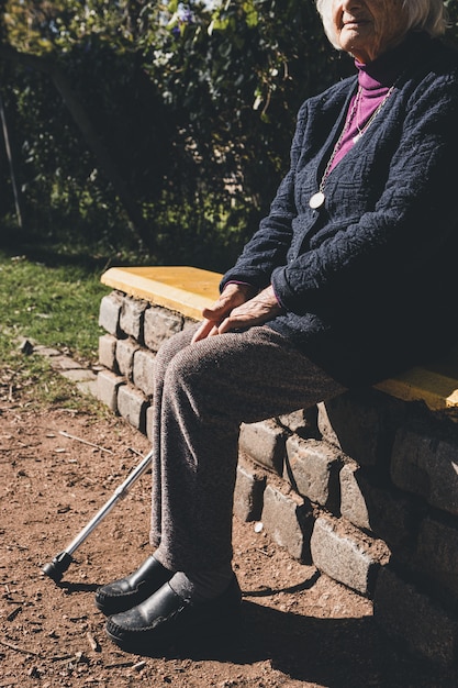 A senior lady sitting on park bench in the sun.
