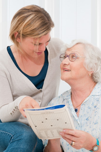 Senior lady solving crosswords puzzle with the help of her young granddaughter at home