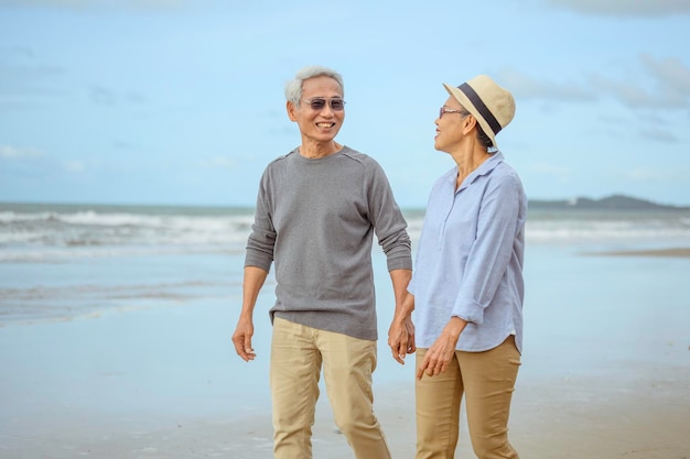 Senior lovers walk hand in hand at the beach at sunrise, plan life insurance at retirement concept.