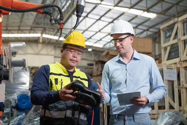 Senior male automation engineer explain using control for robot\
arm welding machine at factory