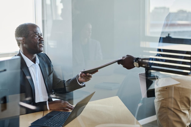 Senior male director of corporation taking document from hand of subordinate