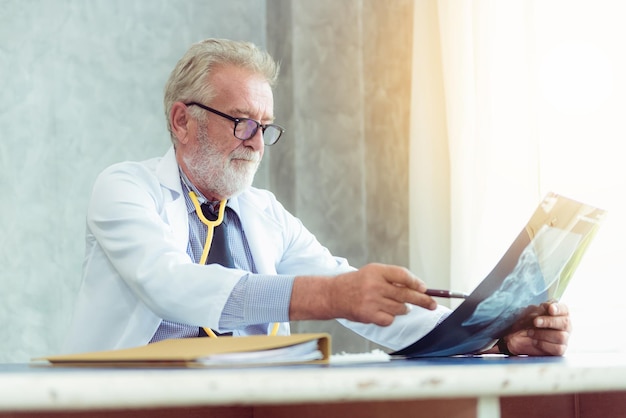 Senior male doctor examining x-ray at desk in hospital