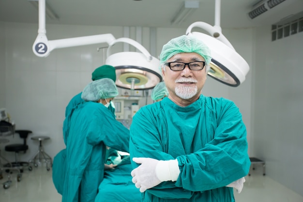 Foto medico maschio senior che guarda alla macchina fotografica con il sorriso attraente al fondo della sala operatoria.