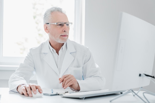 Senior male doctor in office using desktop computer