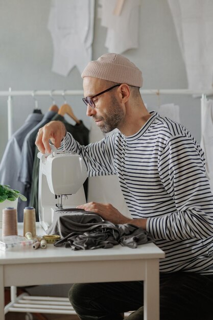 Photo senior male fashion designer or clothing constructor sews on a sewing machine in the workshop and