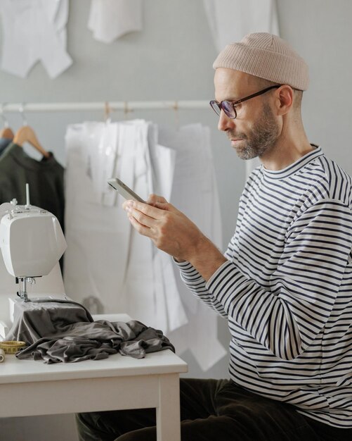 Senior male fashion designer or clothing constructor sews on a sewing machine in the workshop and