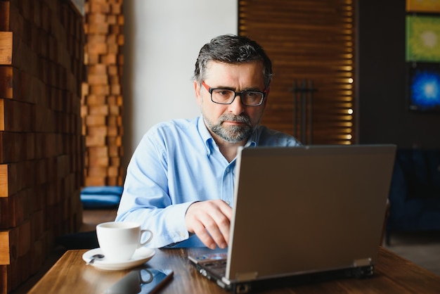 Libero professionista maschio senior che lavora al computer portatile nel concetto di lavoro a distanza del caffè