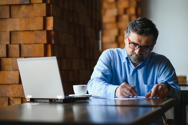 Senior male freelancer working on laptop in cafe remote work concept