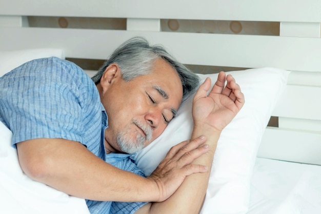朝のライフスタイルで白いベッドの枕の上で寝ている年配の男性老人シニア男性健康コンセプト