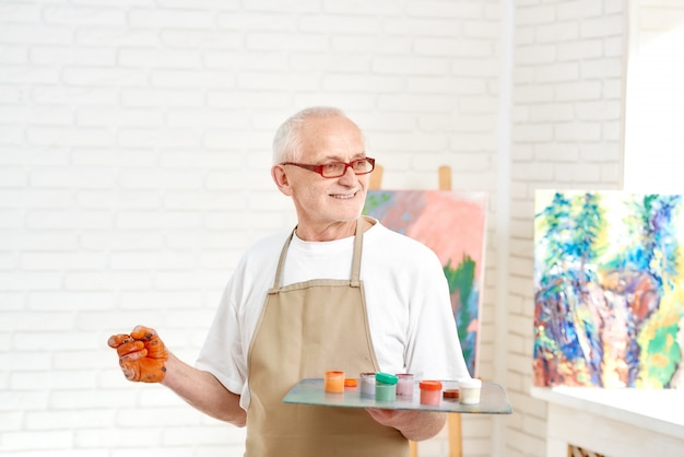 Photo senior male painter, standing with palette of colors in hand, picking up paint to picture