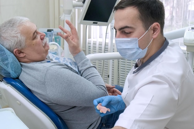 Старший пациент мужского пола консультируется со стоматологом по поводу съемных протезов в стоматологическом кабинете