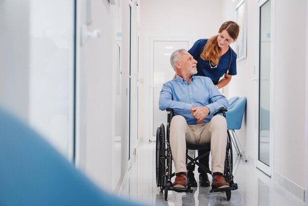 Photo senior male patient sitting in wheelchair in hospital corridor with female nurse doctor