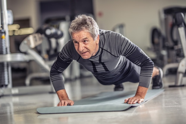 Senior male stays fit by doing pushups on a mat inside the fitness center.