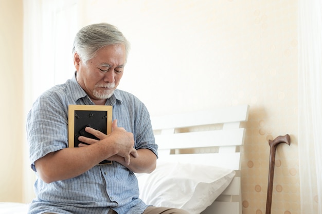 Senior male unhappy is crying, hugging the image of the deceased wife