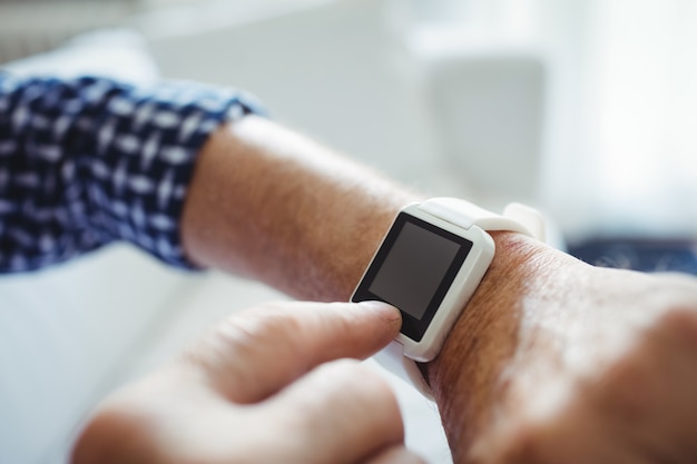 Senior man adjusting a time on smartwatch in living room