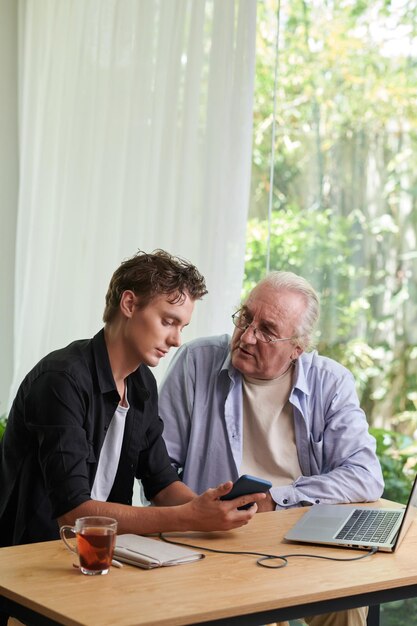 Senior man asking teenage son to install applications on his smartphone