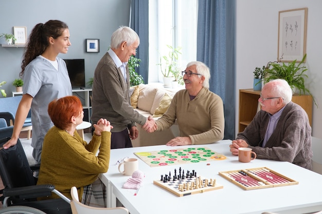 Senior man begroet zijn vrienden in de kamer, ze komen samen om samen bordspellen te spelen