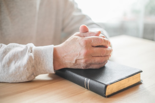 Senior man bidden, een oude bijbel lezen in zijn handen.