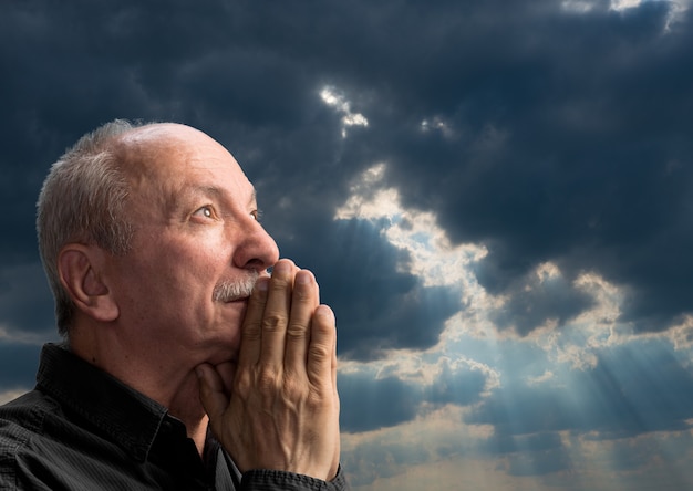 Senior man bidt tegen blauwe bewolkte hemel