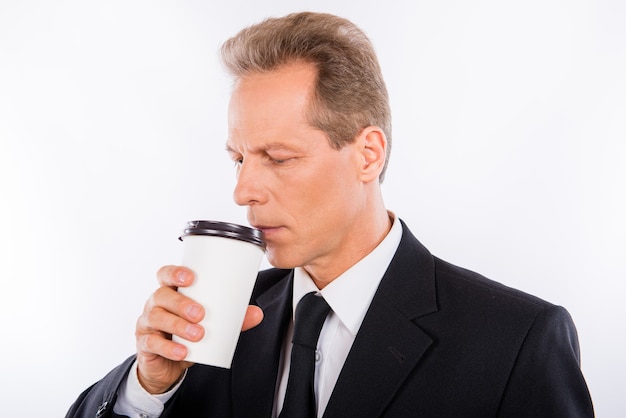 A senior man in a black suit drinks coffee