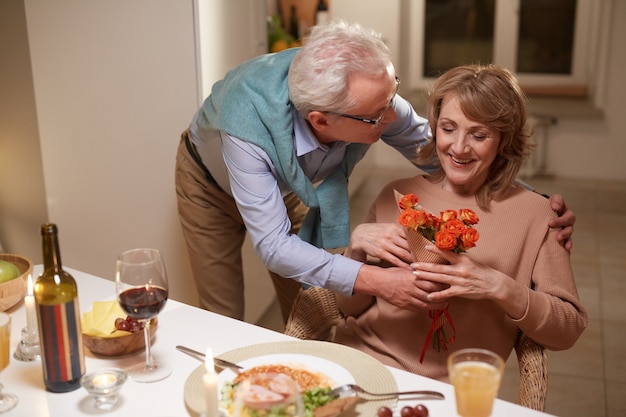 Senior man bloemen geven aan zijn vrouw en haar feliciteren met hun verjaardag tijdens het diner