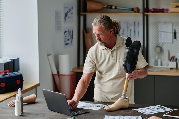 Senior man building leg prosthetics and using laptop