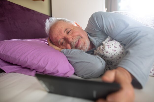 朝のベッドでタブレットのニュースをチェックする年配の男性