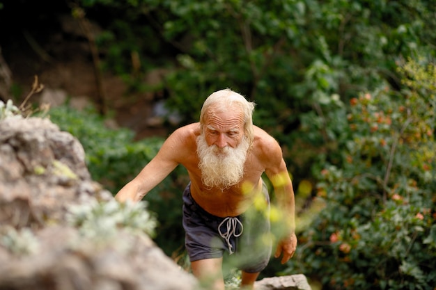 Uomo anziano che si arrampica sulla roccia. nonno con una lunga barba bianca