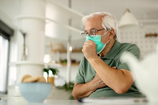 Senior man coughing while wearing protective face mask at home