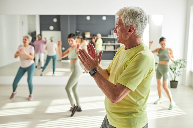 Senior man dancing during sport training with other people in background