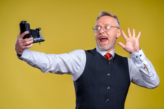 Senior man die naar de camera kijkt terwijl hij een dwaas gezicht selfie neemt. Zwaaien naar de camera