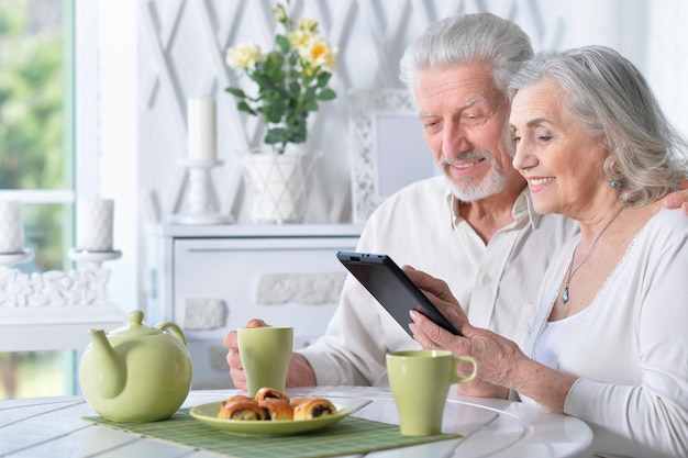 Senior man die tablet gebruikt terwijl hij thee drinkt