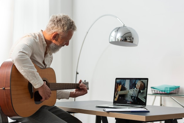 Foto senior man die thuis gitaarlessen studeert op laptop