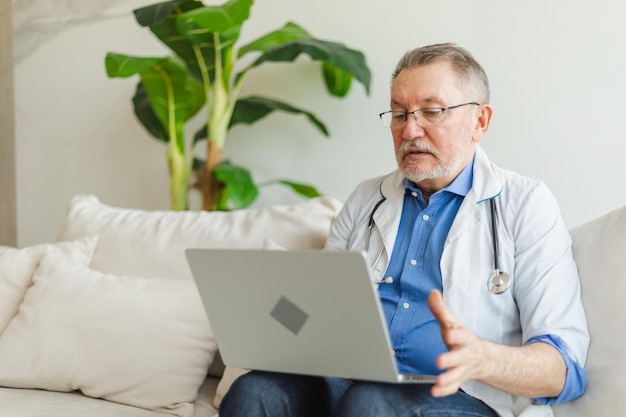 Foto un medico anziano con un portatile parla su video-call ha una consultazione con un paziente professionista anziano