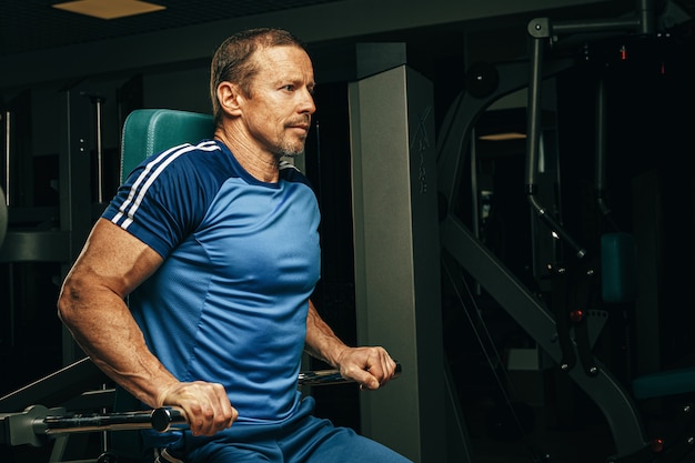 Senior man doing exercises for arms in a training machine in gym