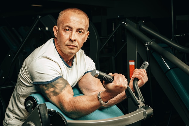 Senior man doing exercises for arms in a training machine in gym